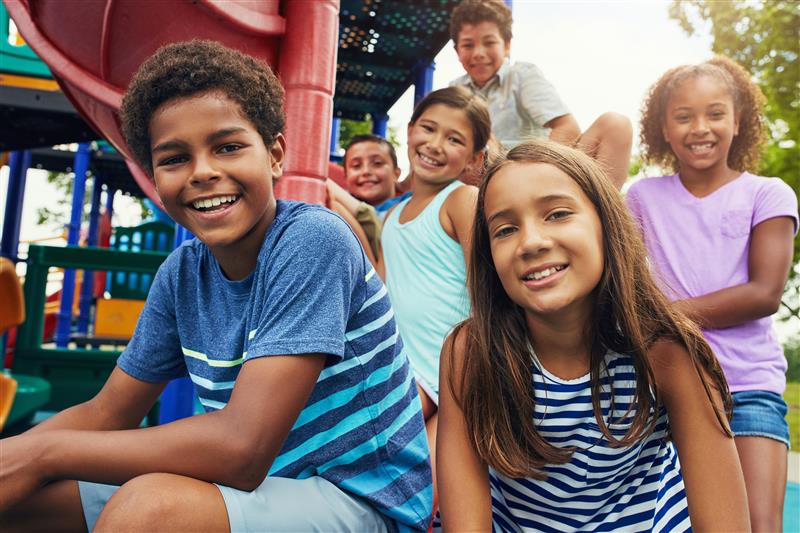 Children sitting on playground slide smiling, multiple ages and races