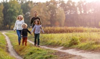 A family walking together along a grassy path in a sunlit field with trees in the background 