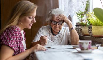 Woman and Elderly Woman with pen in hand sitting at a table looking at some papers