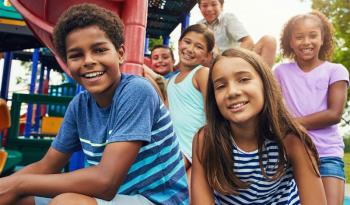Children sitting on playground slide smiling, multiple ages and races